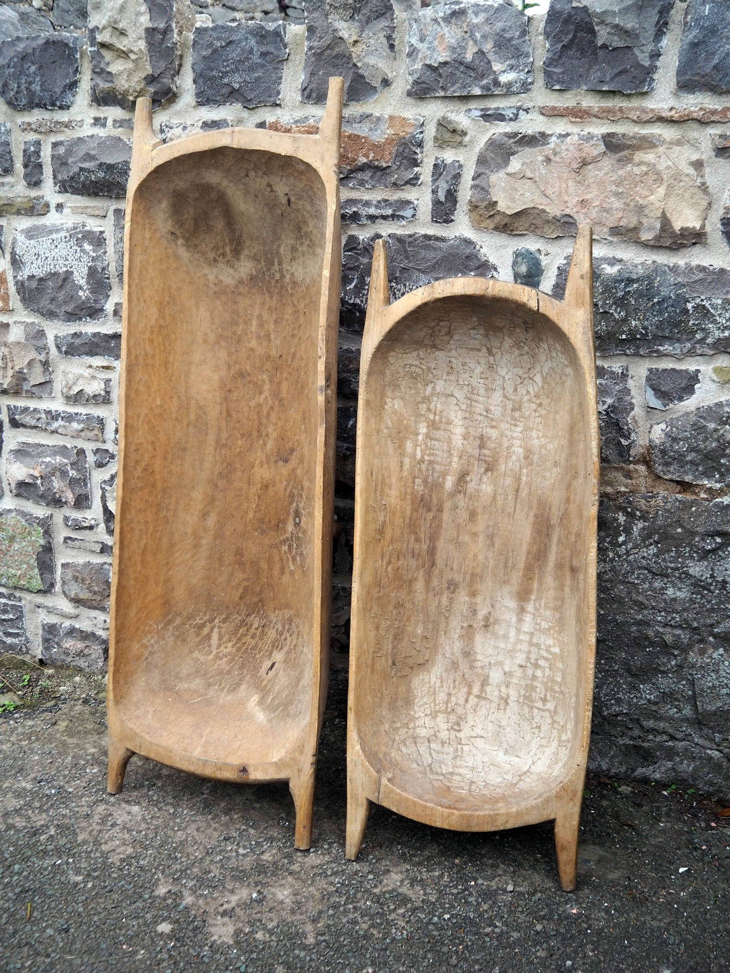Two wooden antique doughbowls leaning against a stone wall.