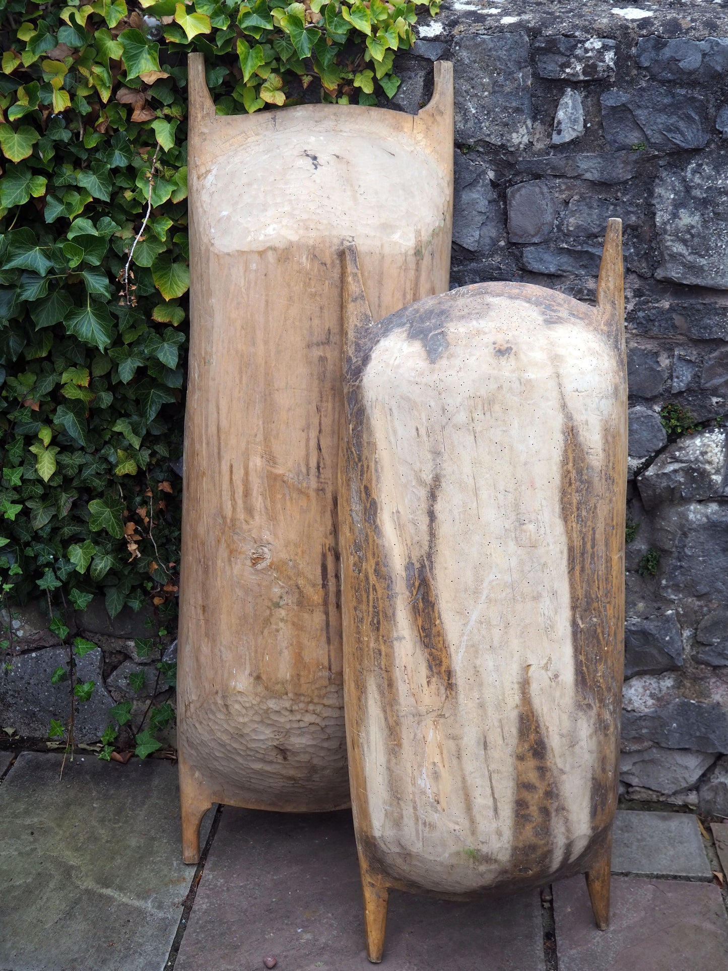 Two large wooden planters against a stone wall with greenery