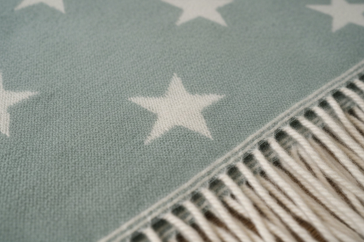 Green blanket with white star patterns and fringe on a wooden surface