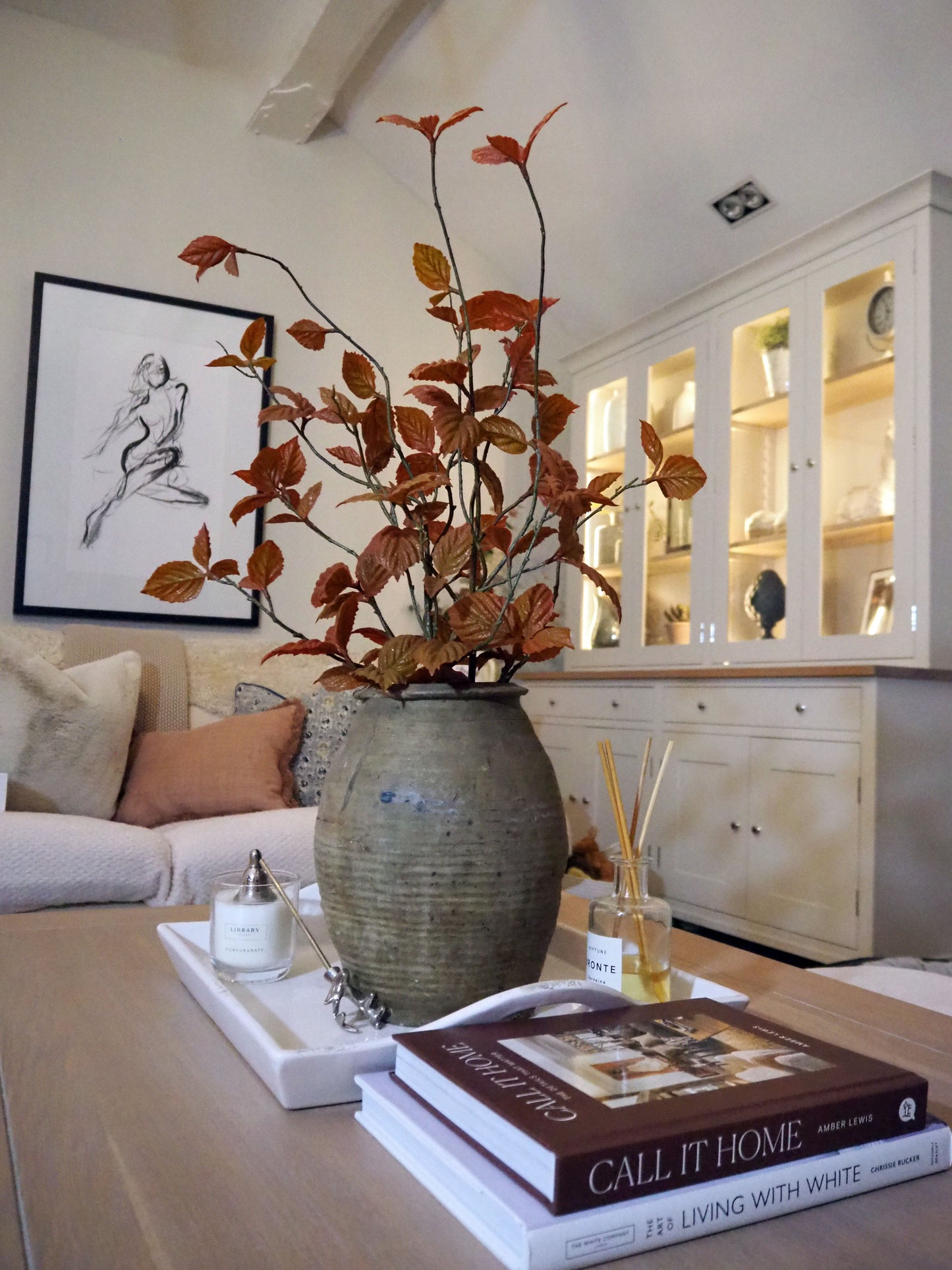 Decorative vase with red leaves on a coffee table in a living room setting.