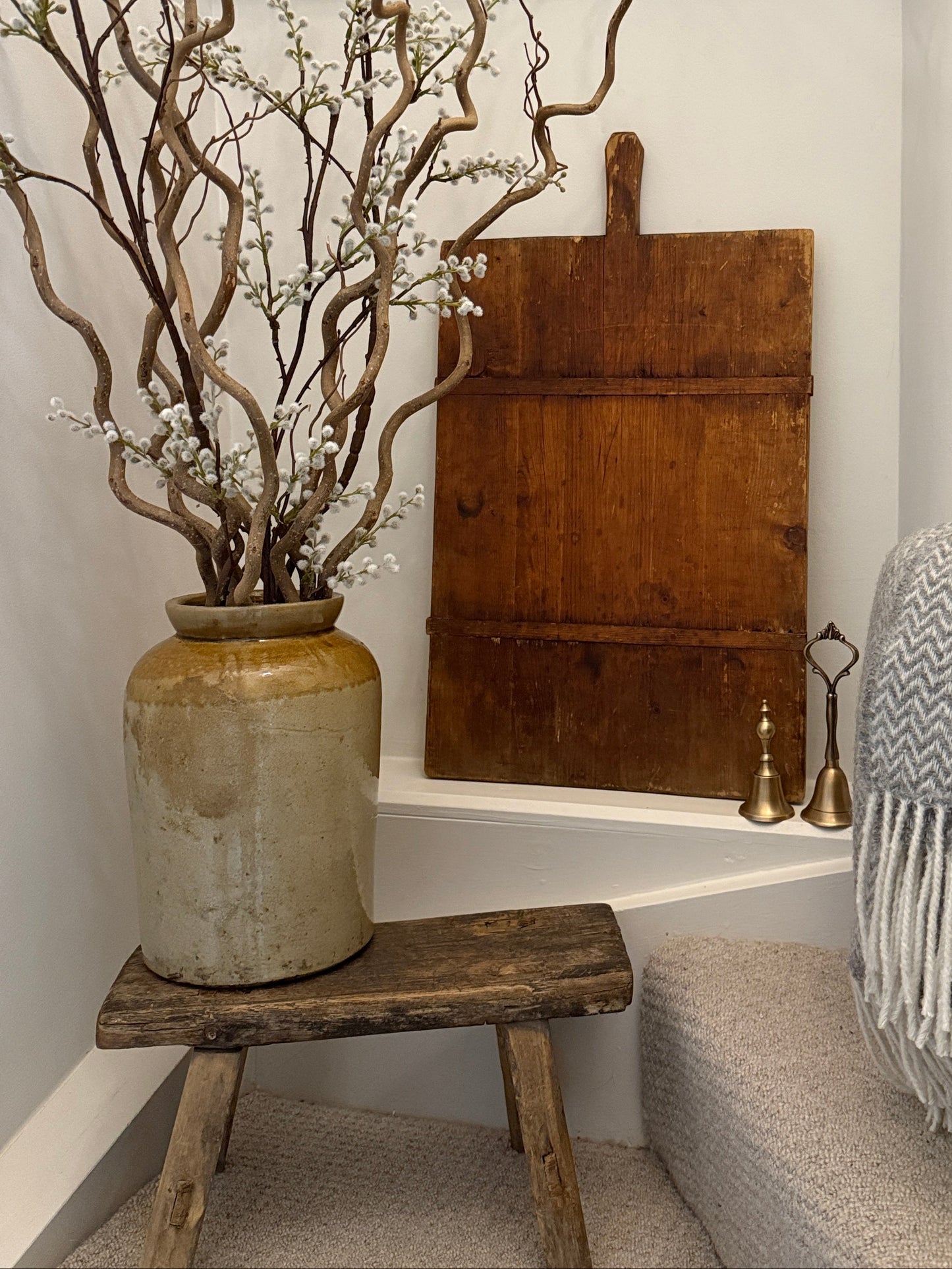 Decorative elements including a vase with branches, a wooden French bread board, and a textured Welsh throw all from TYFFI Home