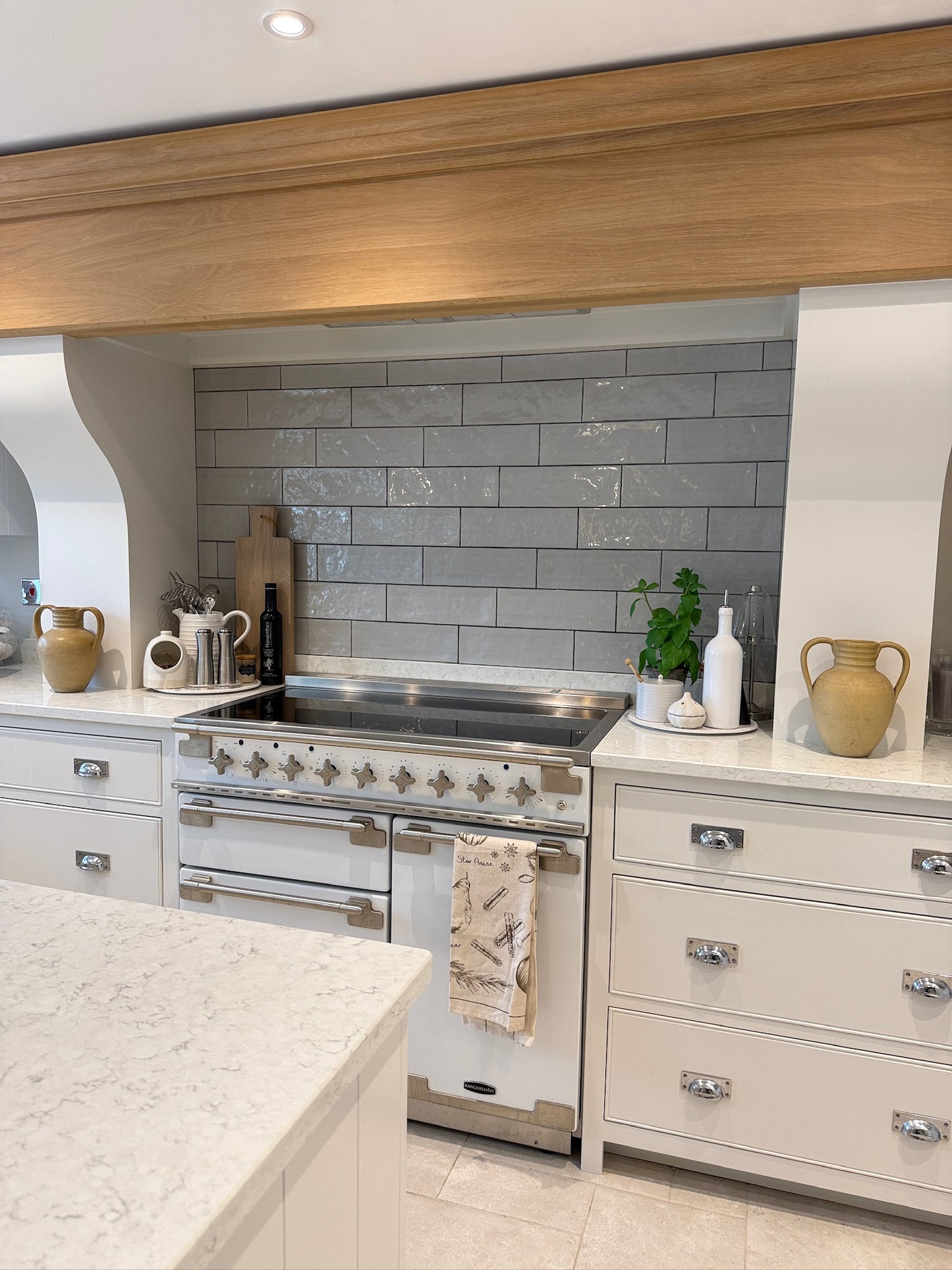 Modern kitchen with stainless steel oven, gray tiled wall, and white countertops.