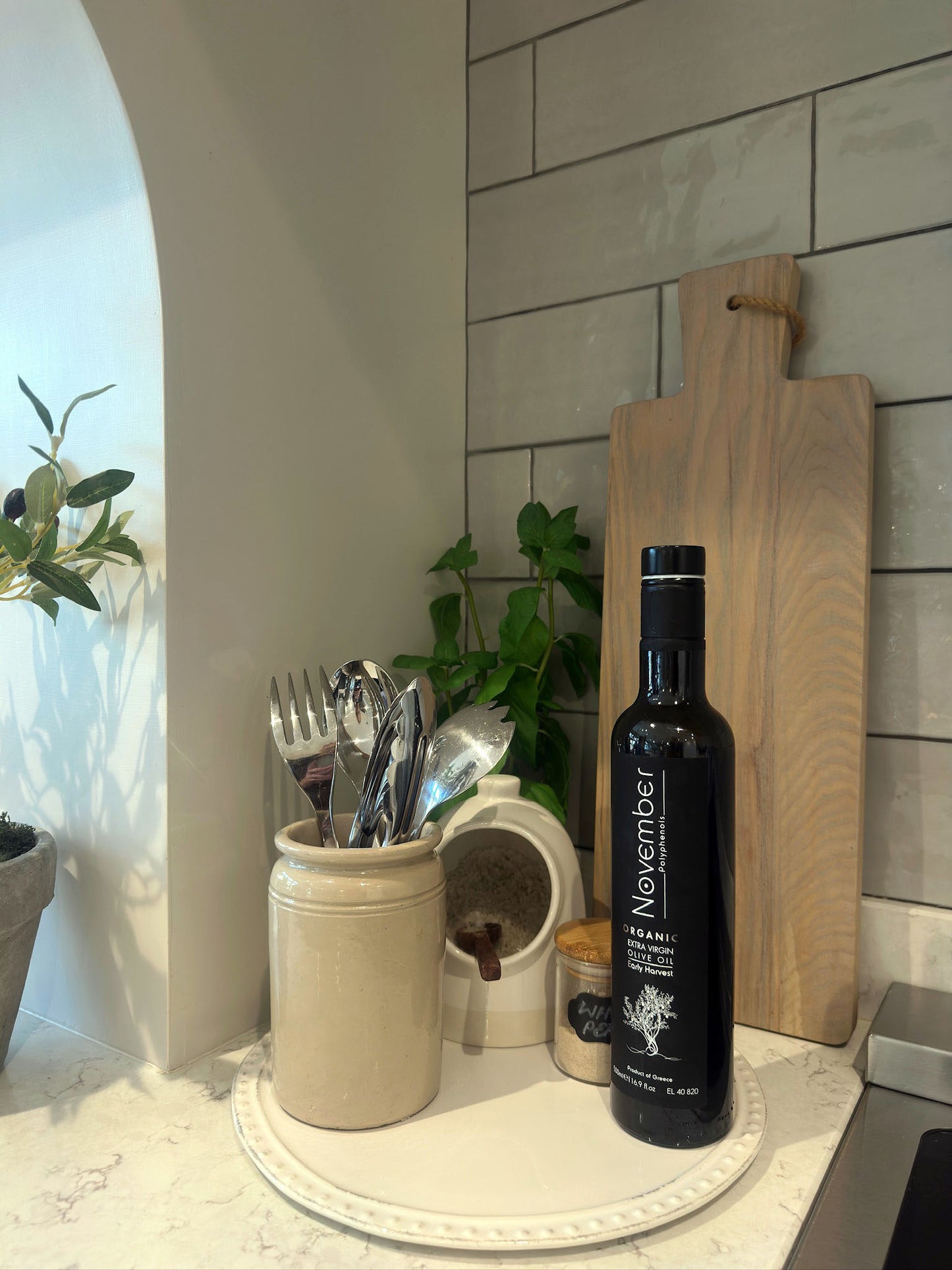 Bottle of olive oil on a kitchen counter with utensils and a cutting board.
