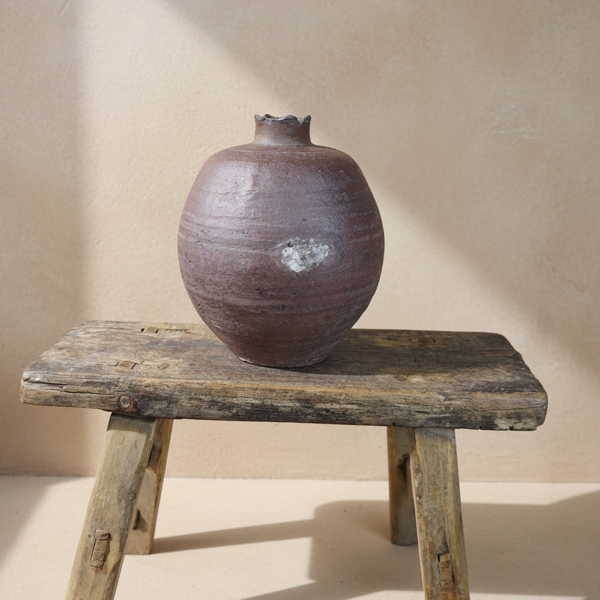 Purple ceramic vase on a wooden stool against a plain background