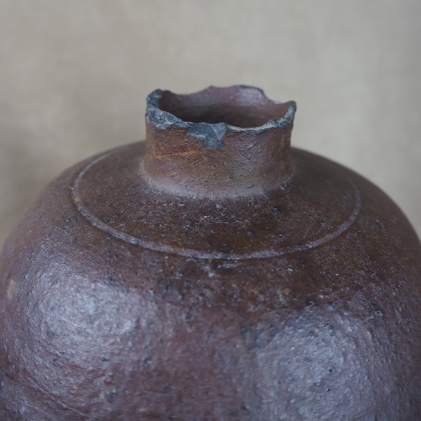 Close-up of a dark brown ceramic pot with a textured surface on a beige background