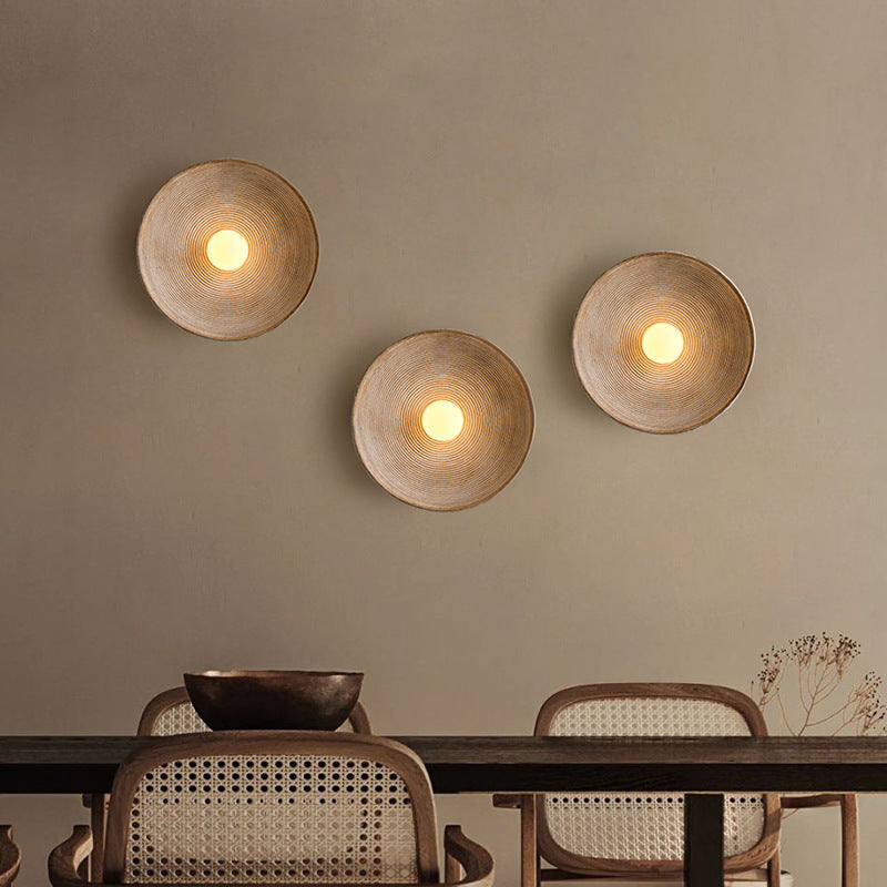 Three wall-mounted round lights on a beige wall above a dining table with chairs.