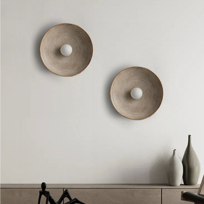 Two round wall decorations on a light gray wall with a shelf below.