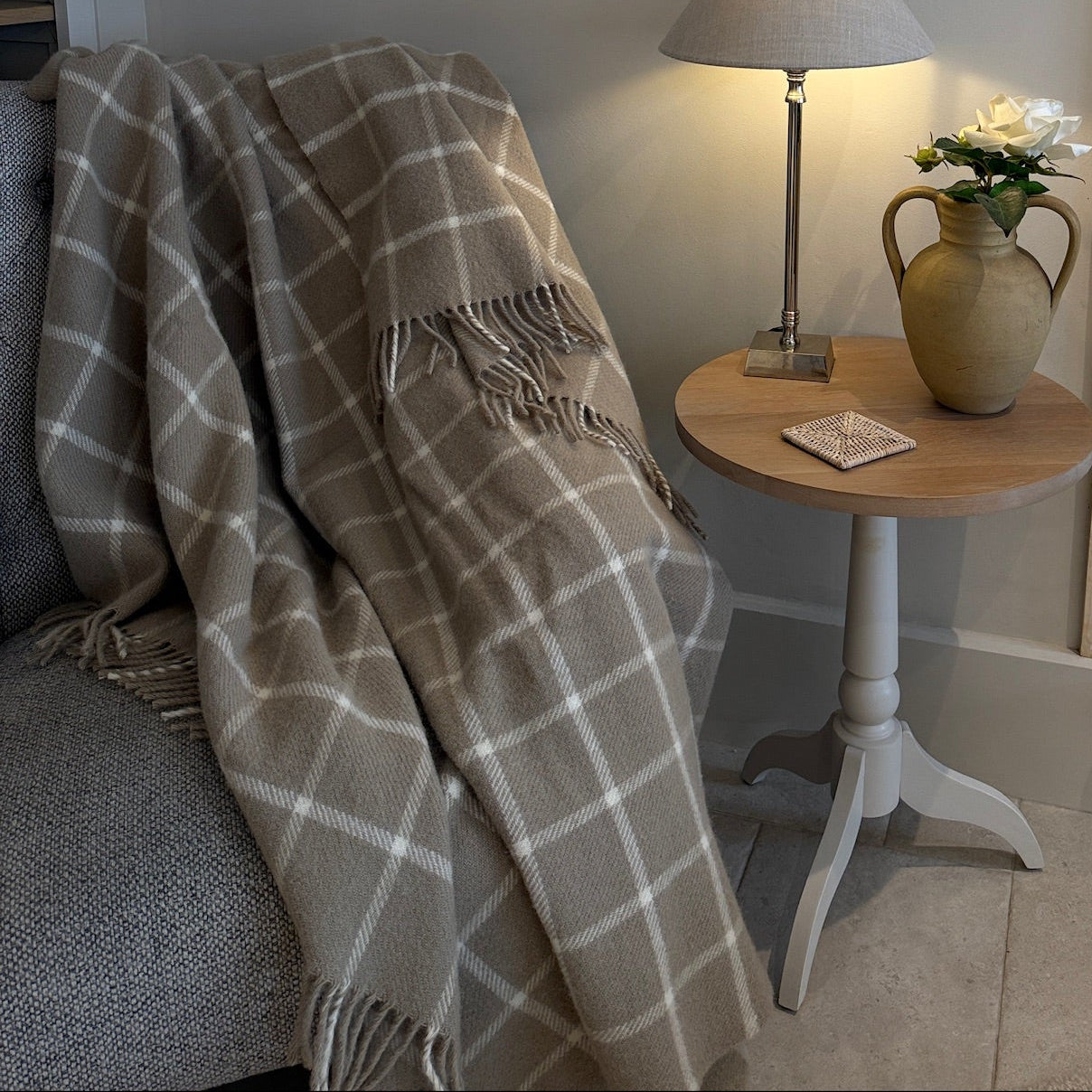 Cozy living room corner with a plaid blanket, lamp, and vase.