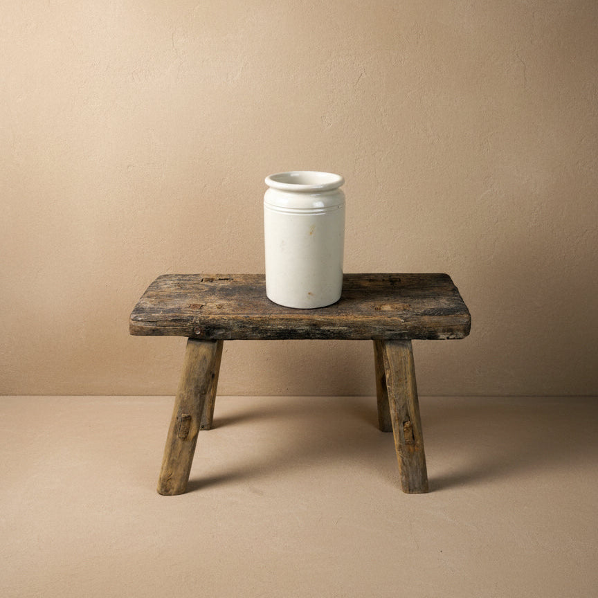 White ceramic jar on a rustic wooden stool against a plain background