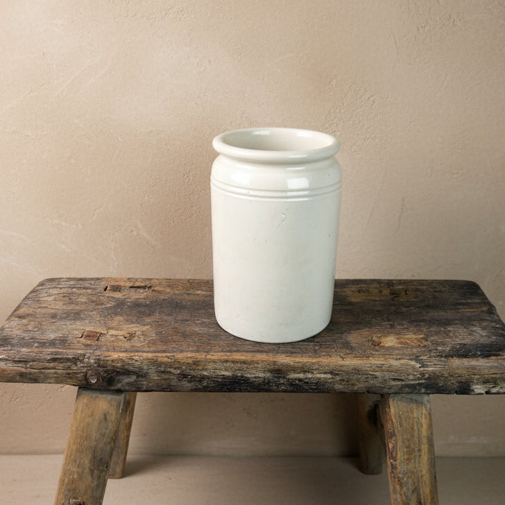 White ceramic jar on a rustic wooden stool against a plain background