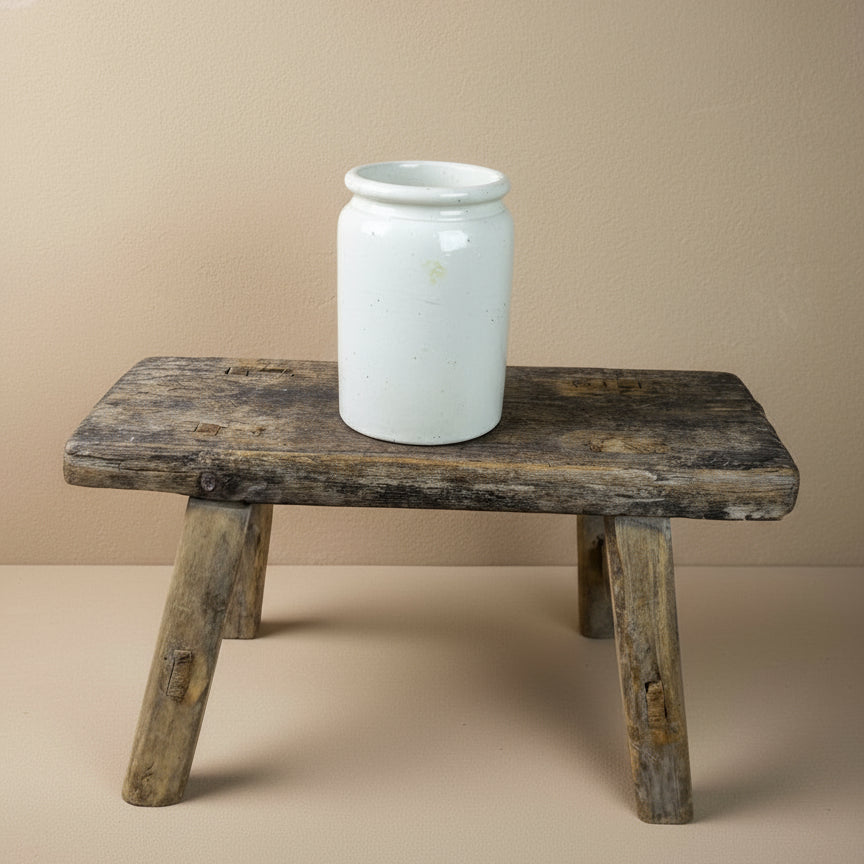 White ceramic jar on a rustic wooden stool against a plain background