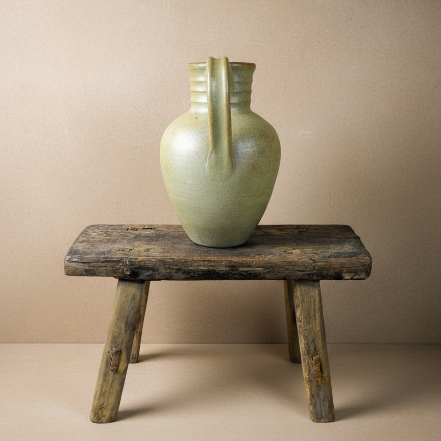 Vintage ceramic pitcher on a rustic wooden stool against a plain background