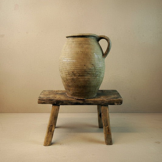 Vintage terracotta jar on a wooden stool against a white background