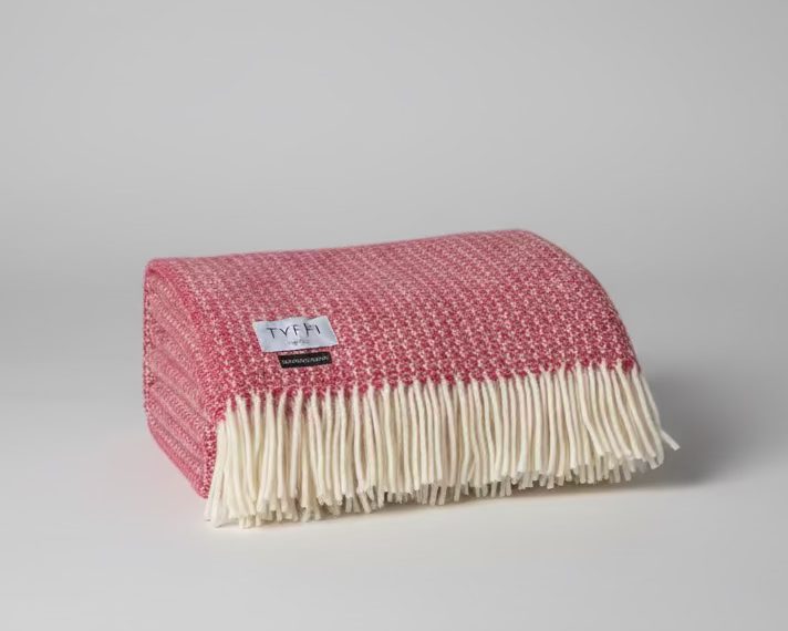 Folded red and white blanket with a visible brand label on a gray background