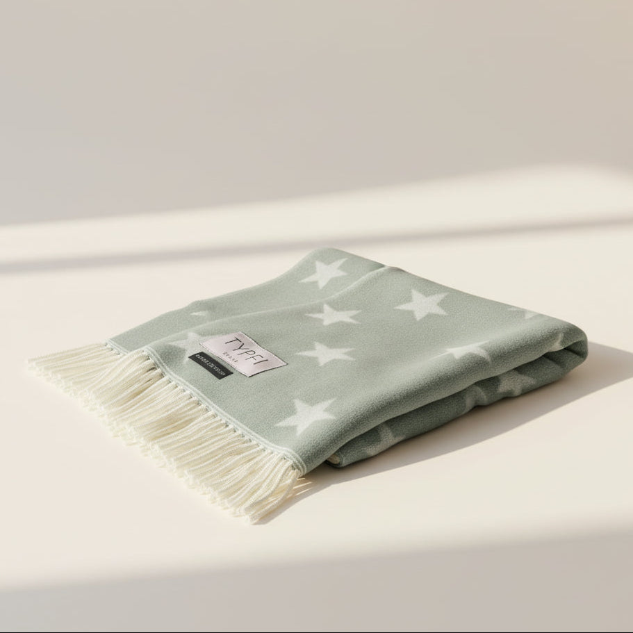 Folded light green blanket with star pattern on a beige surface