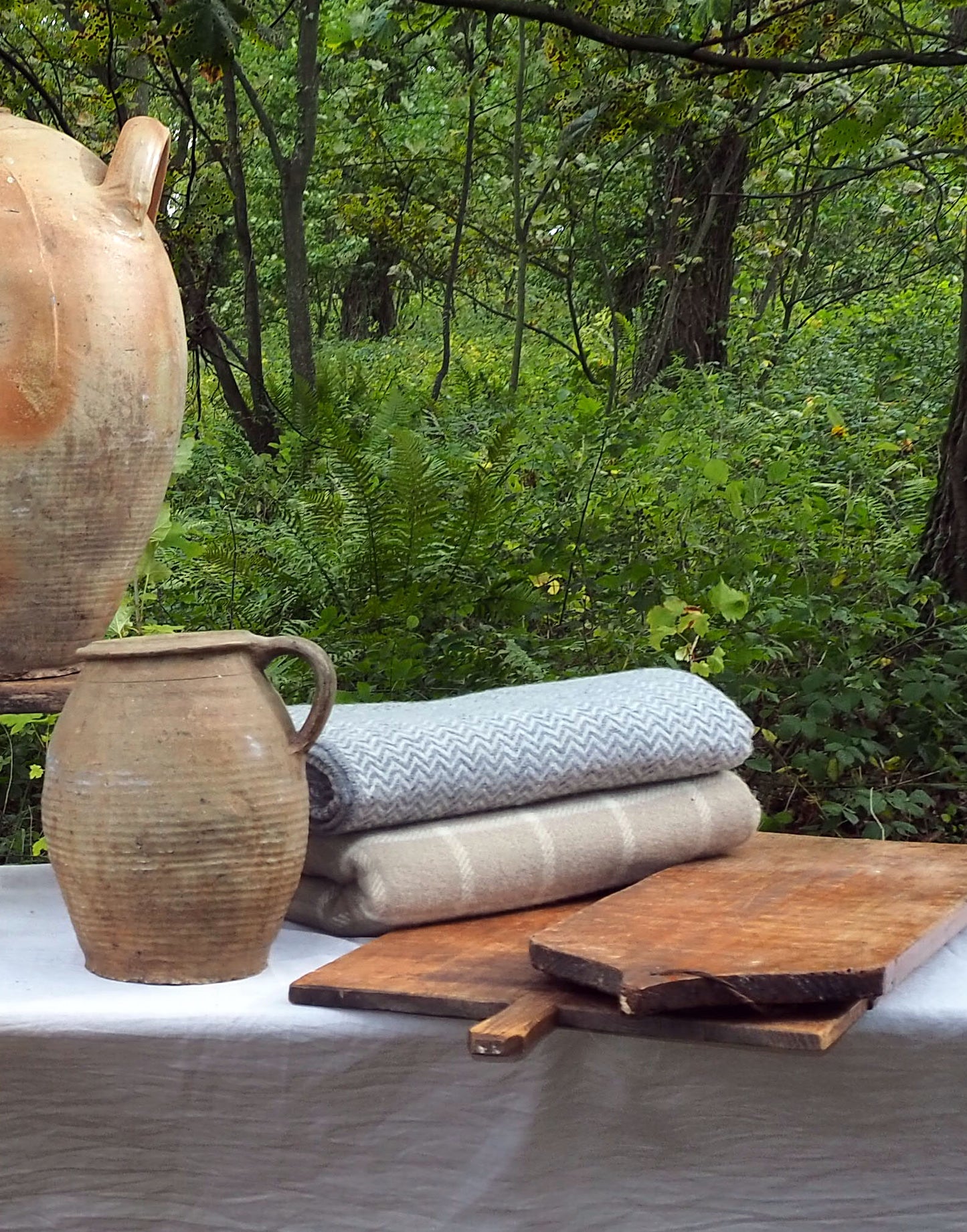 Decorative setting with rustic vases, wooden cutting boards, and folded cloths against a natural background.