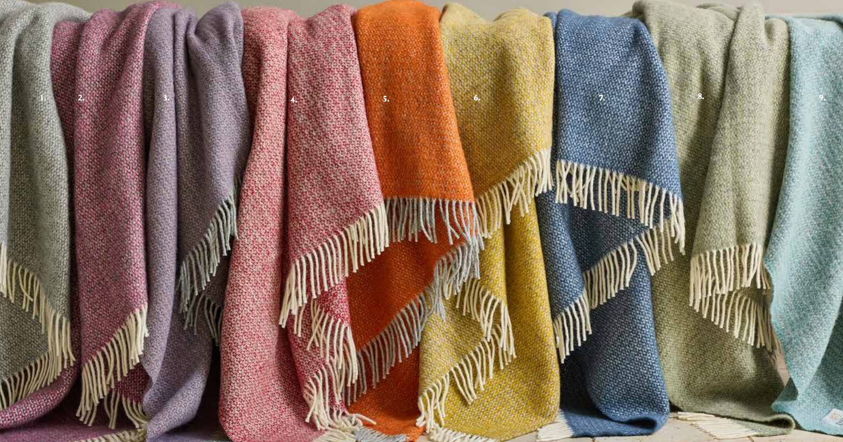 Row of colorful textured blankets with fringes on a neutral background