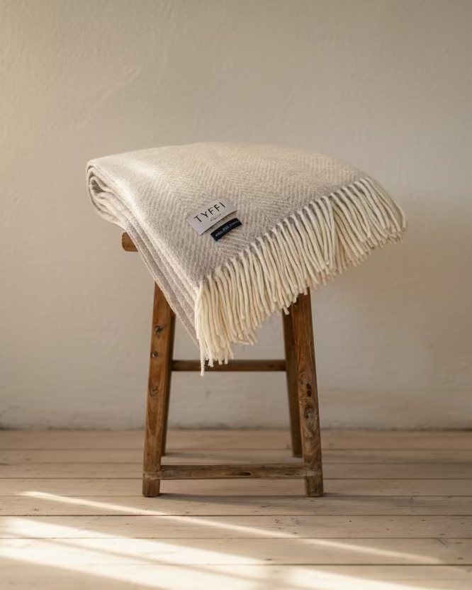 Beige woven blanket on a wooden stool against a gray wall.