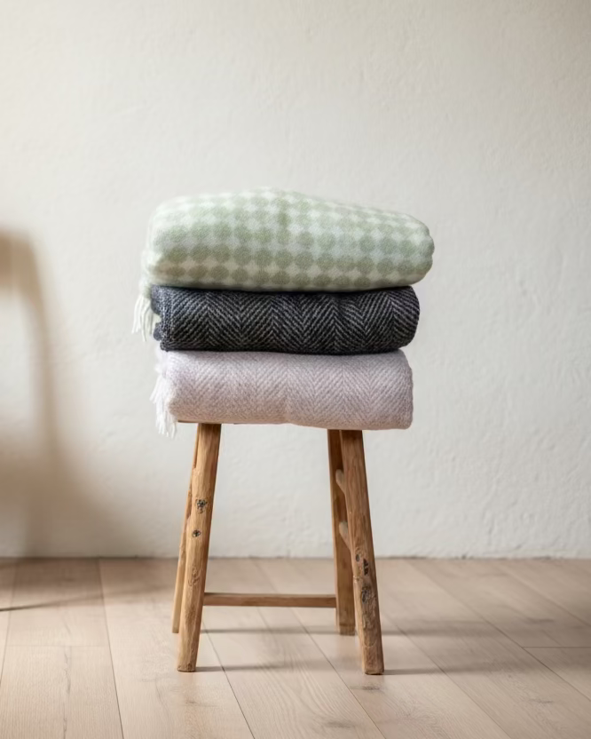 Stack of textured wool blankets on a wooden stool against a plain wall.