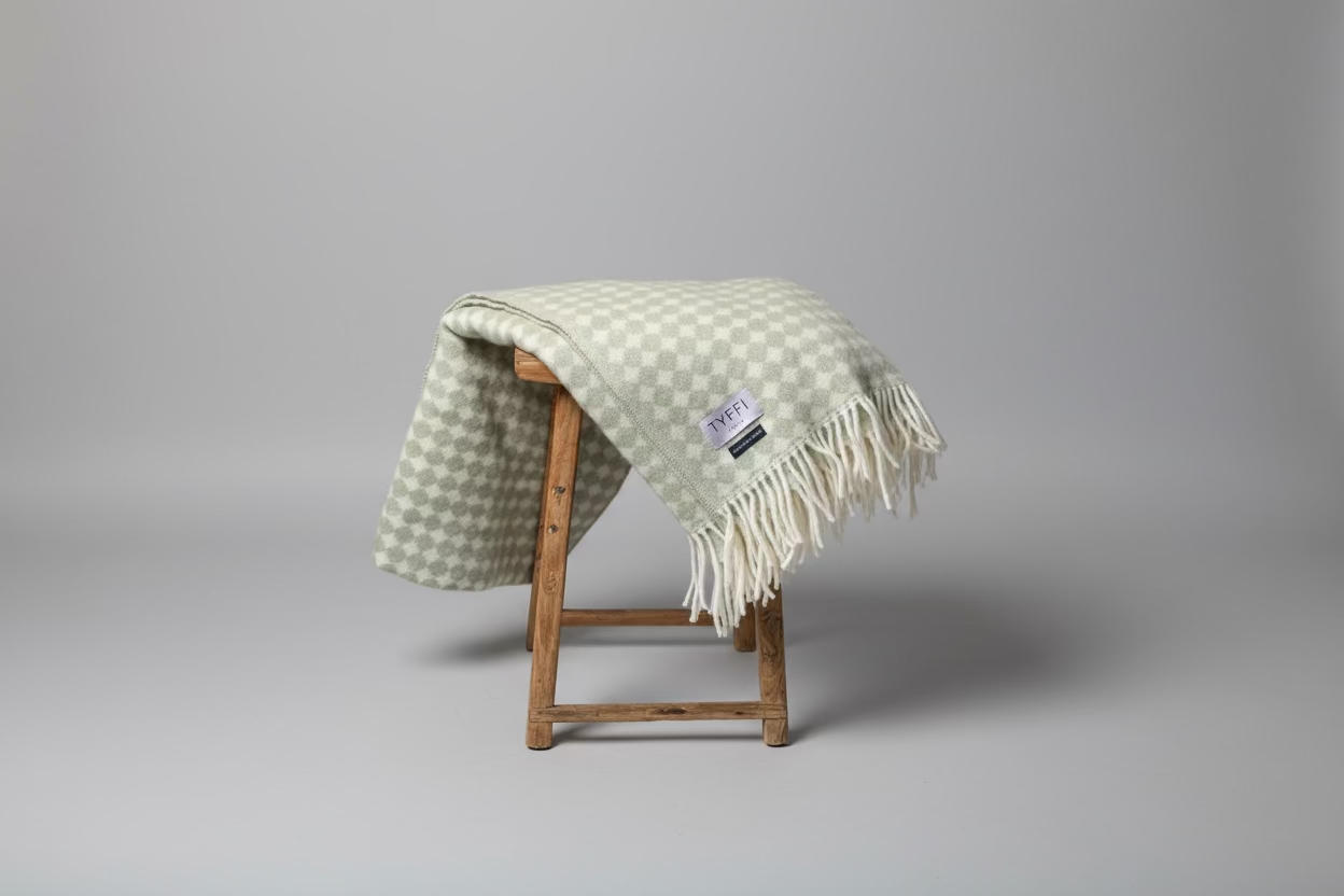 Checkered blanket with tassels on a wooden stool against a gray wall.