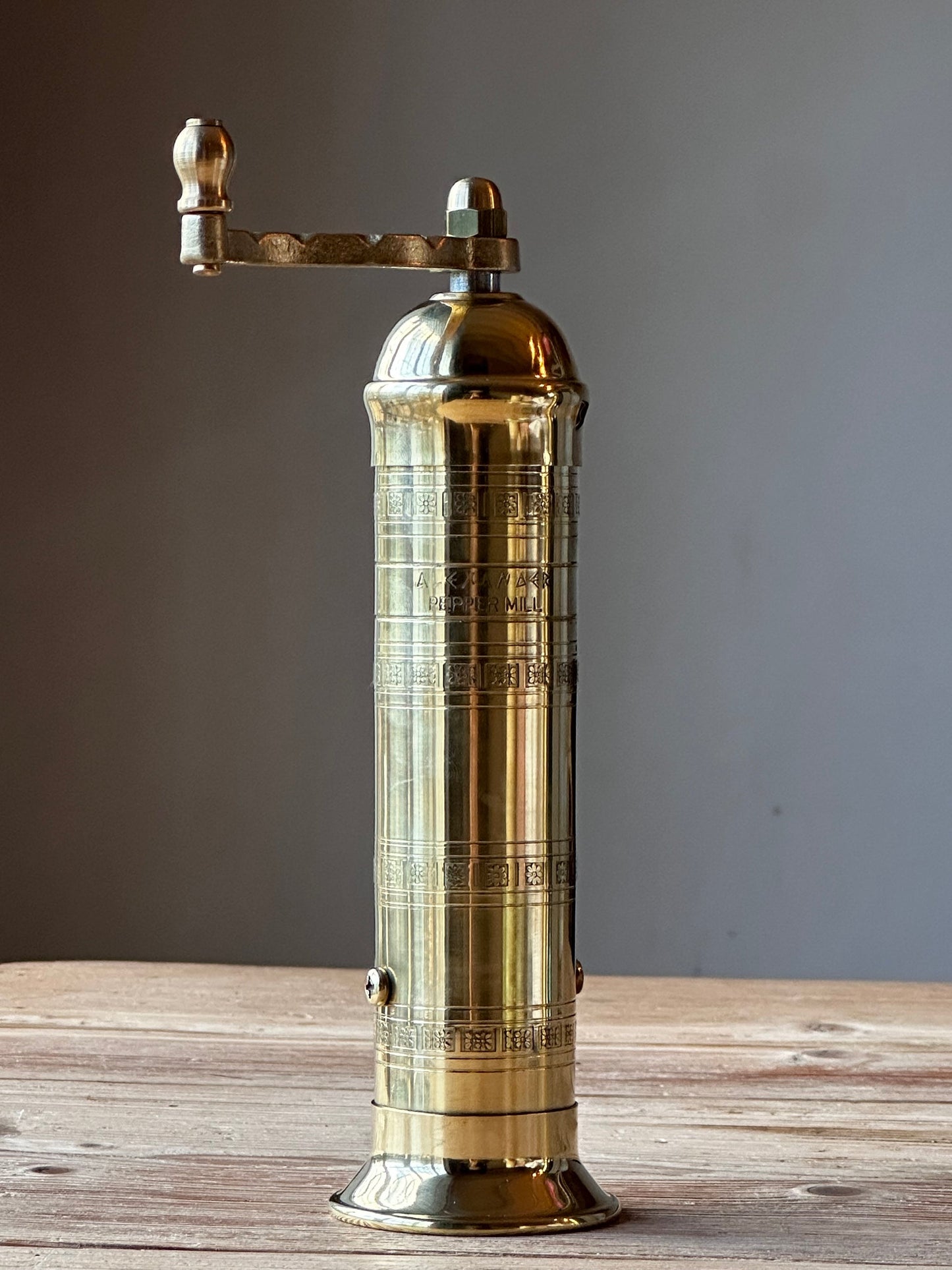 Brass pepper grinder on a wooden surface with a gray background