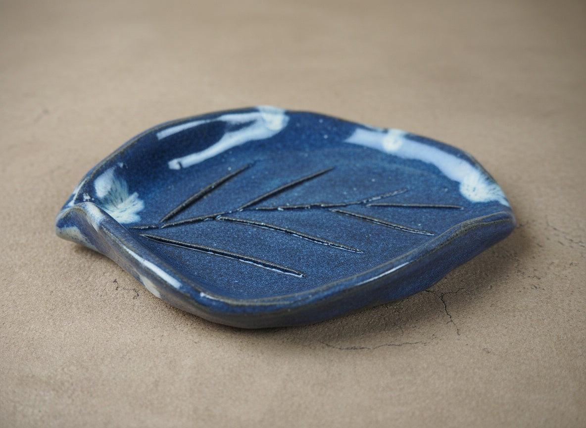 Blue ceramic leaf-shaped dish on a beige surface
