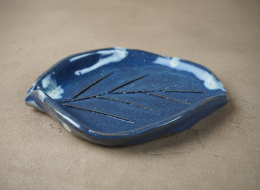 Blue ceramic leaf-shaped dish on a beige surface