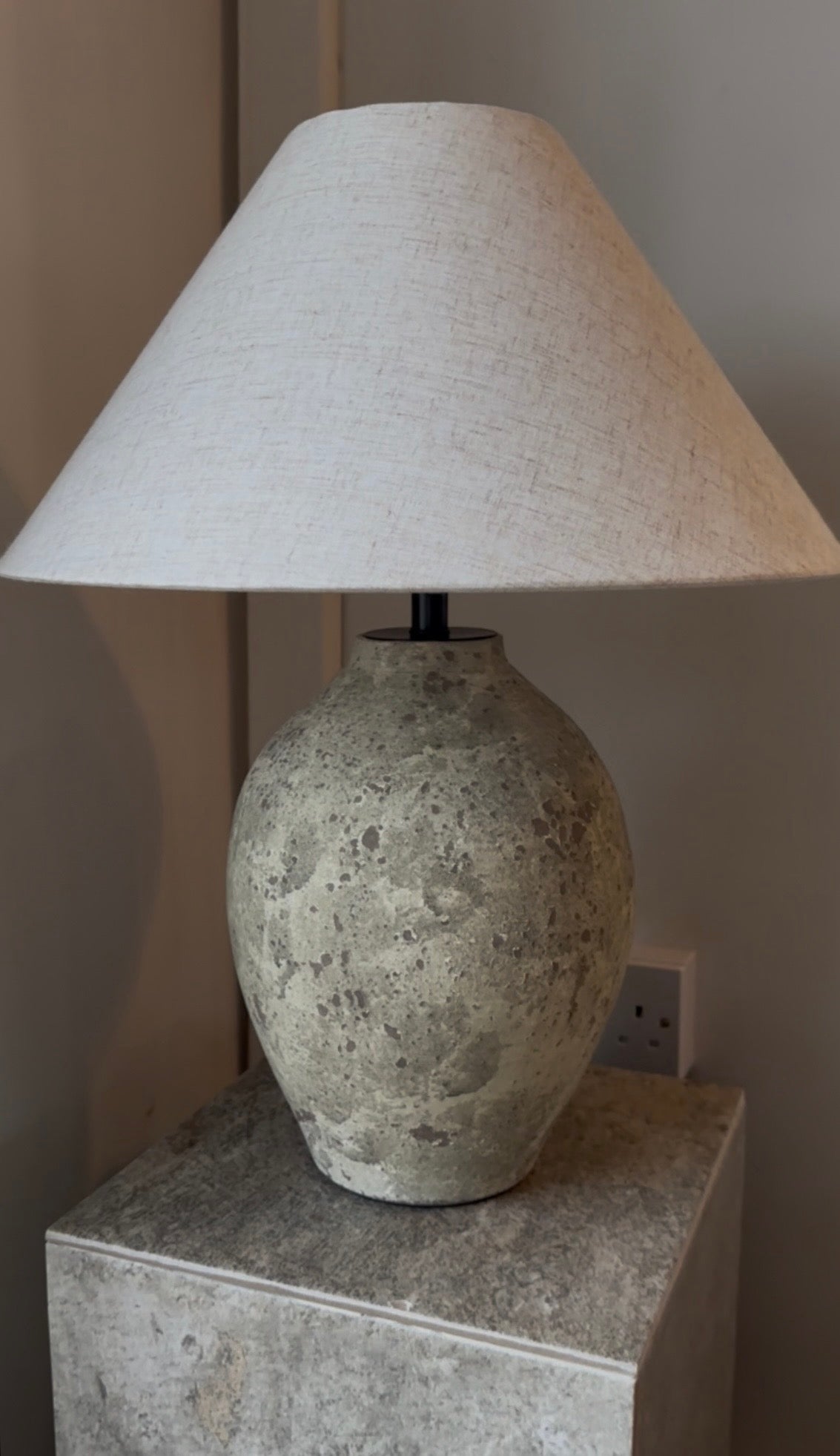 Table lamp with textured concrete base and beige lampshade on a concrete surface.