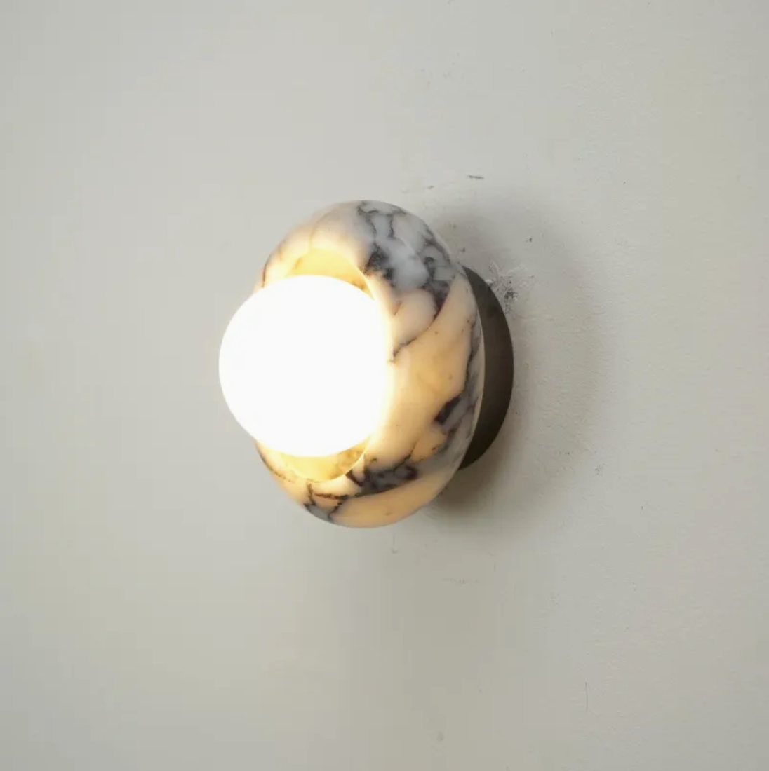 Wall-mounted light fixture with marble design on a plain wall.