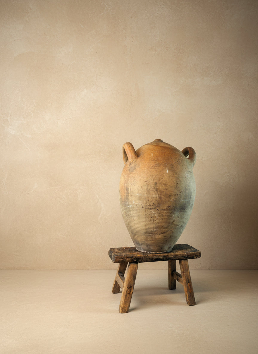 Large terracotta pot on a wooden stool against a plain background