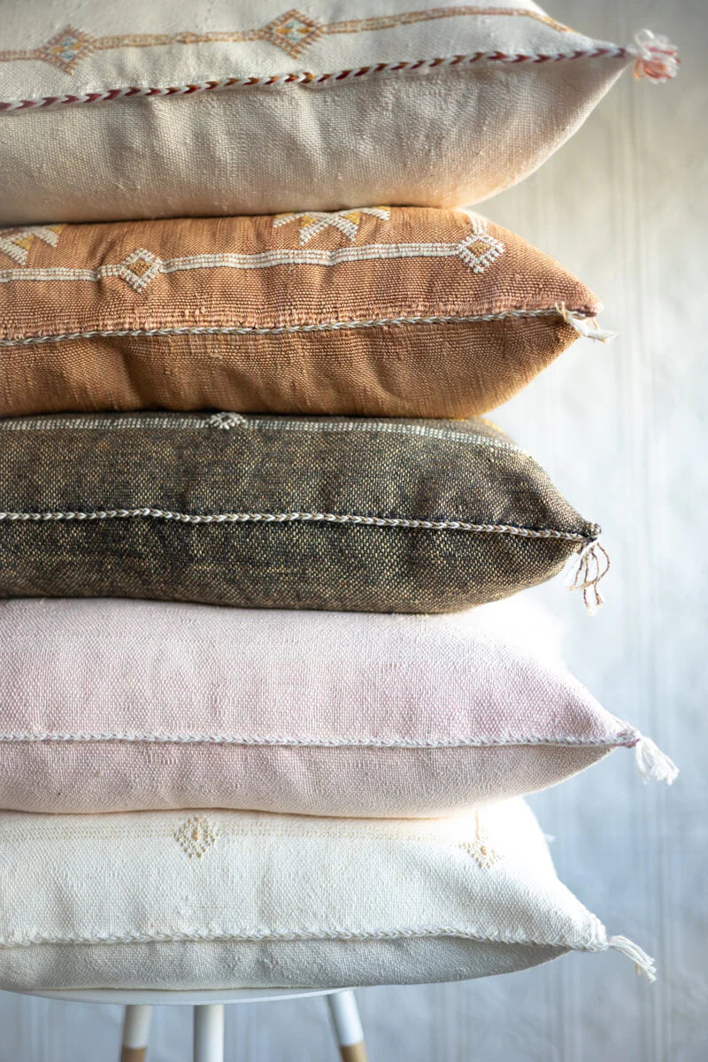 Stack of textured pillows with various colors and patterns on a light background