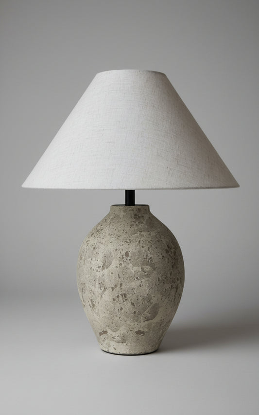 Decorative lamp with textured base and beige lampshade on a concrete surface.