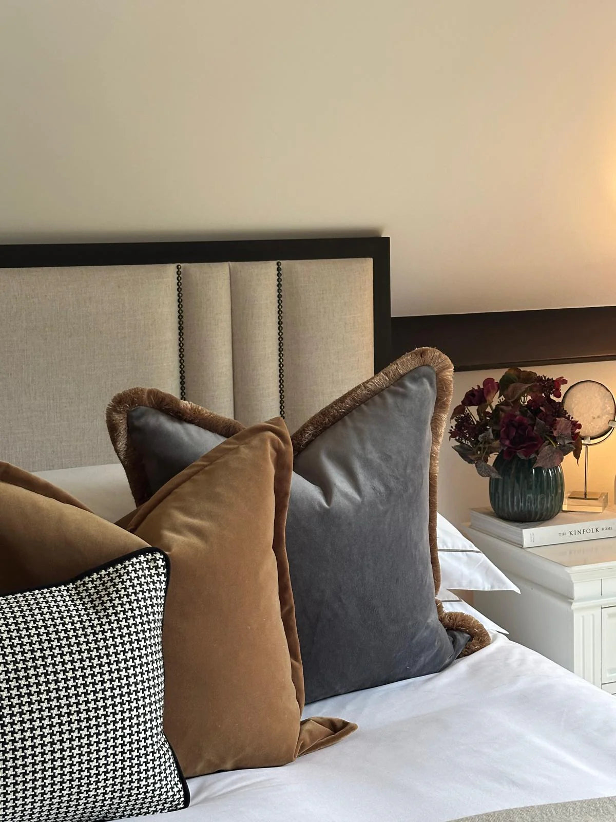 Decorative pillows on a bed with a nightstand and lamp in the background
