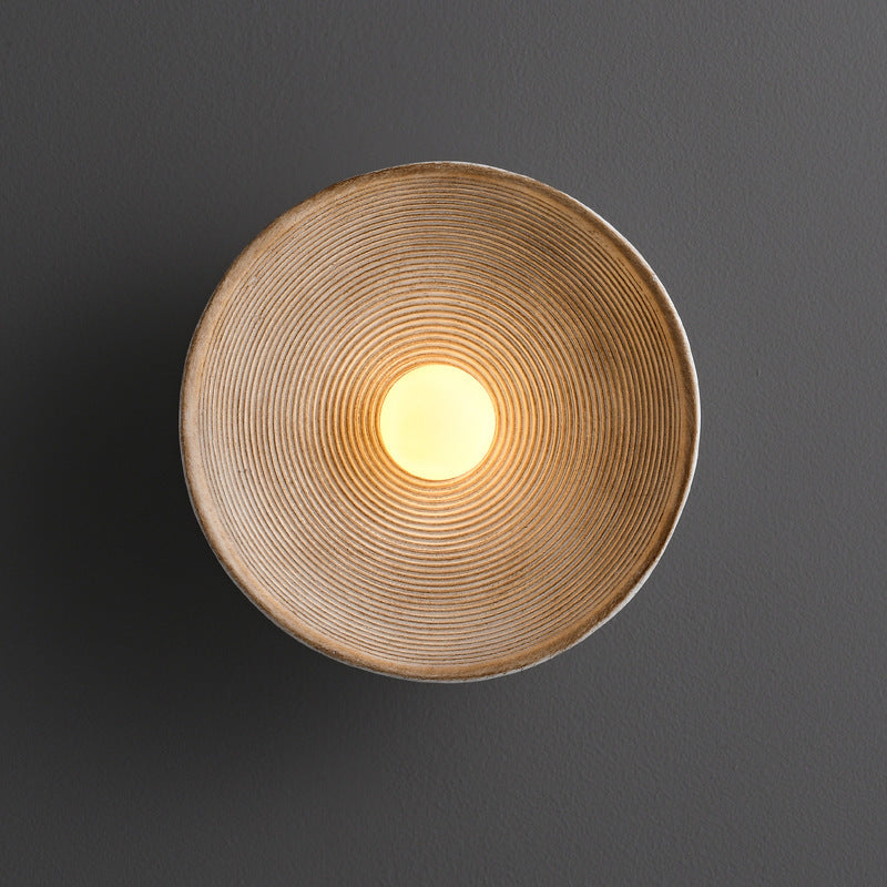 Round wall light fixture with a textured design on a dark background