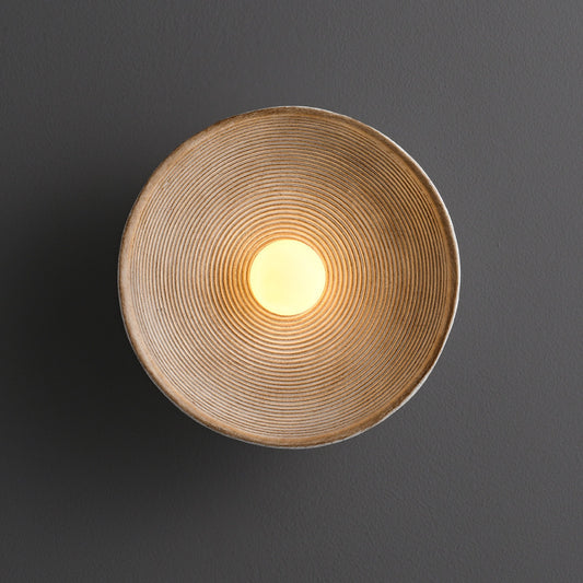 Round wall light fixture with a textured design on a dark background