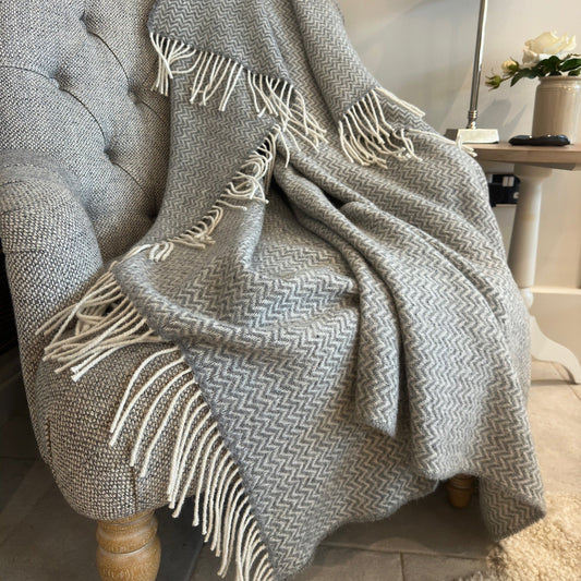 Gray textured wool throw blanket with white fringe draped over a chair in a cozy room.