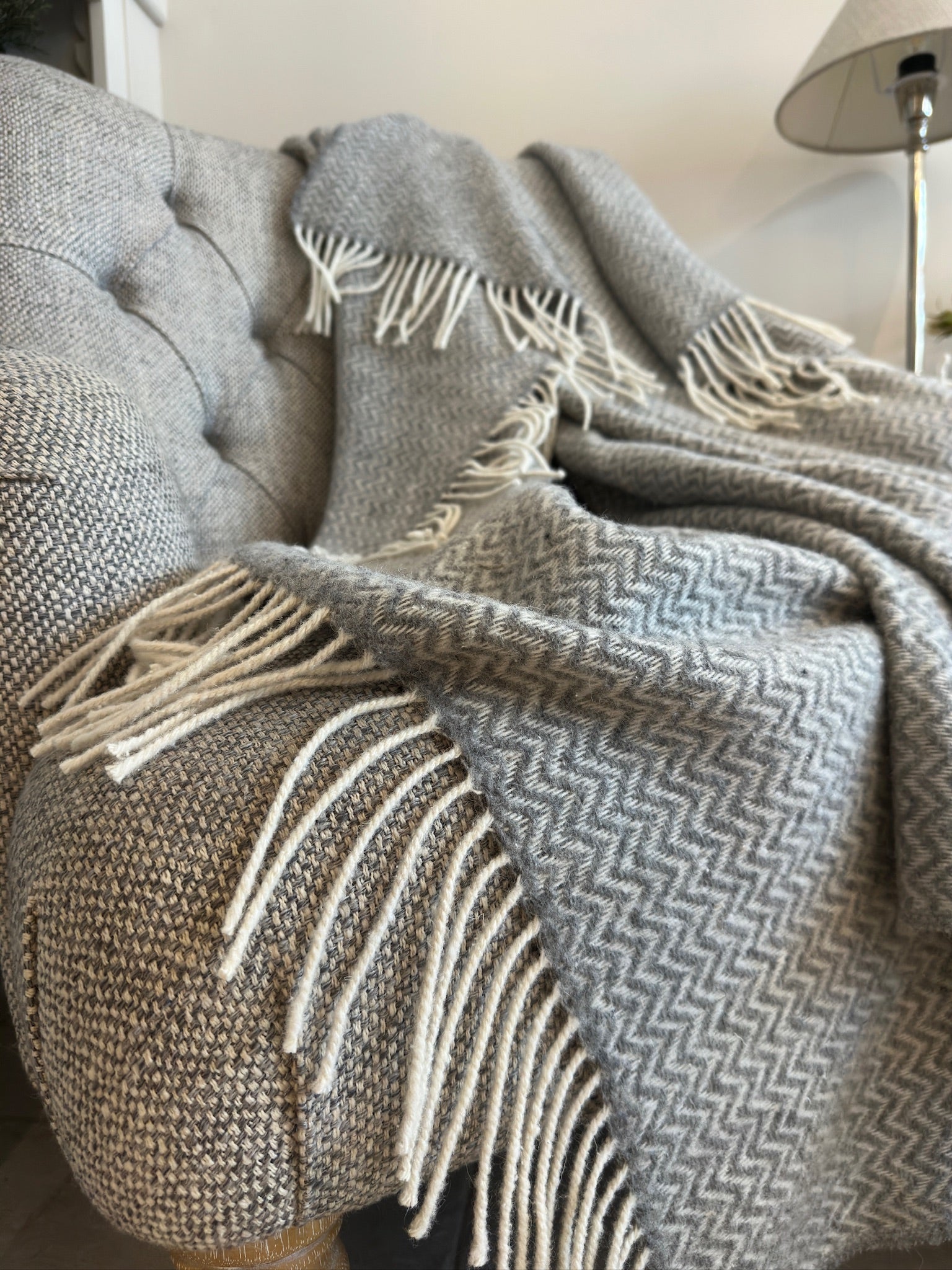 Gray herringbone blanket with white fringe draped over a textured surface.