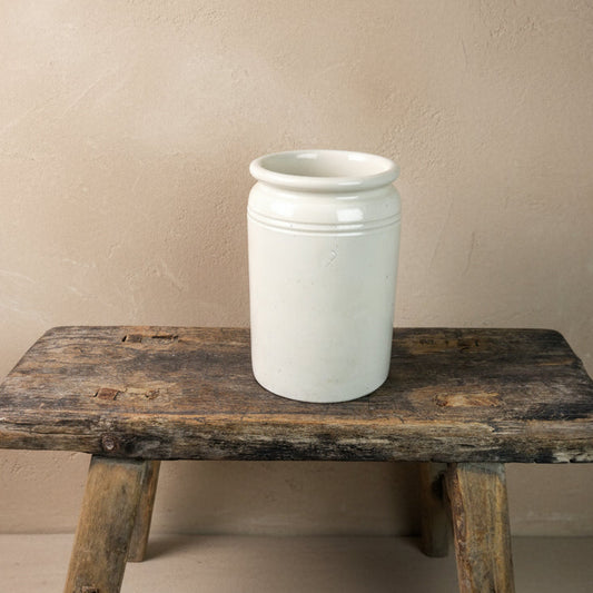 White ceramic jar on a rustic wooden stool against a plain background