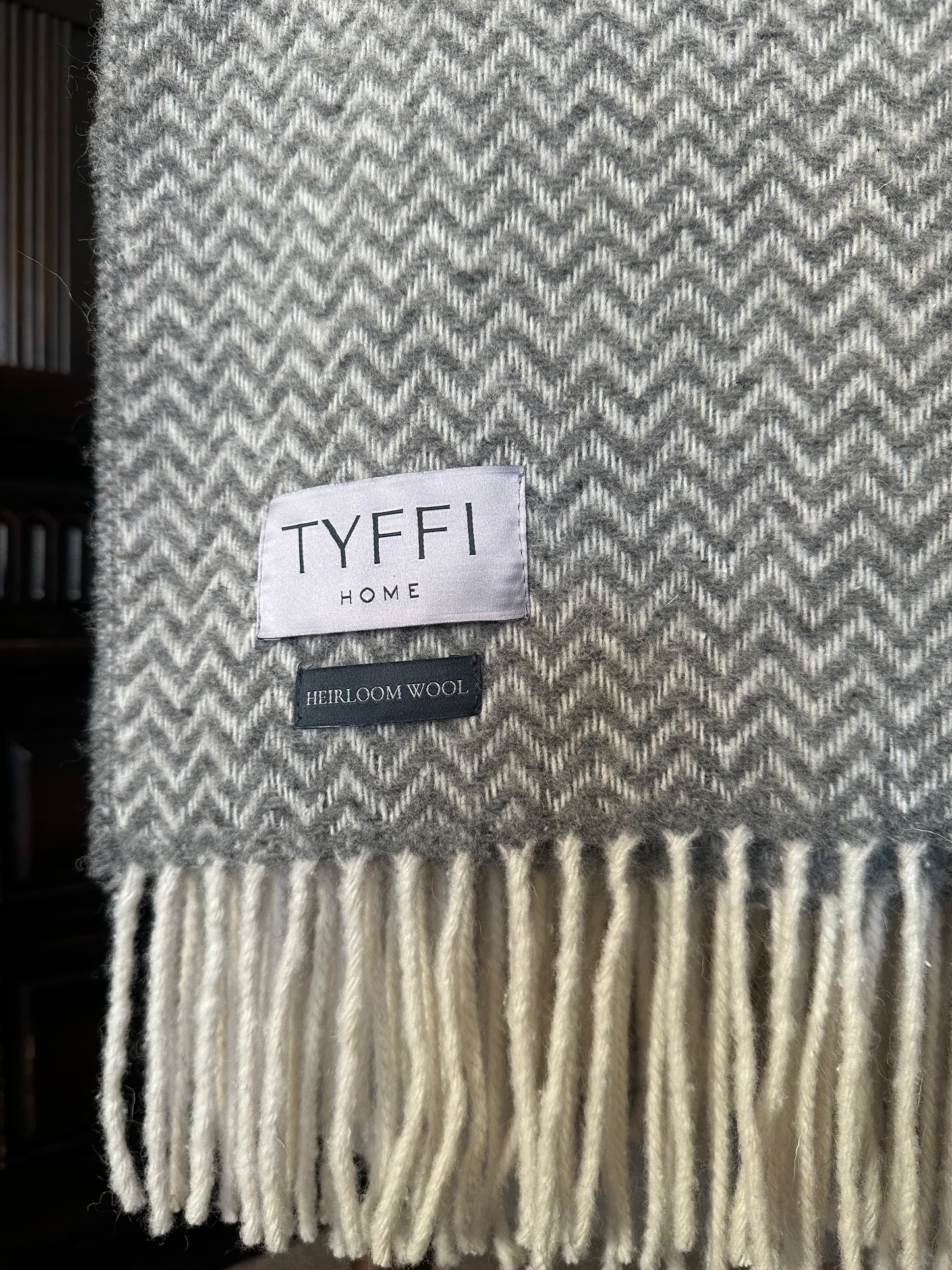 Gray and white herringbone patterned throw blanket with 'TYFFI HOME' label on a dark background