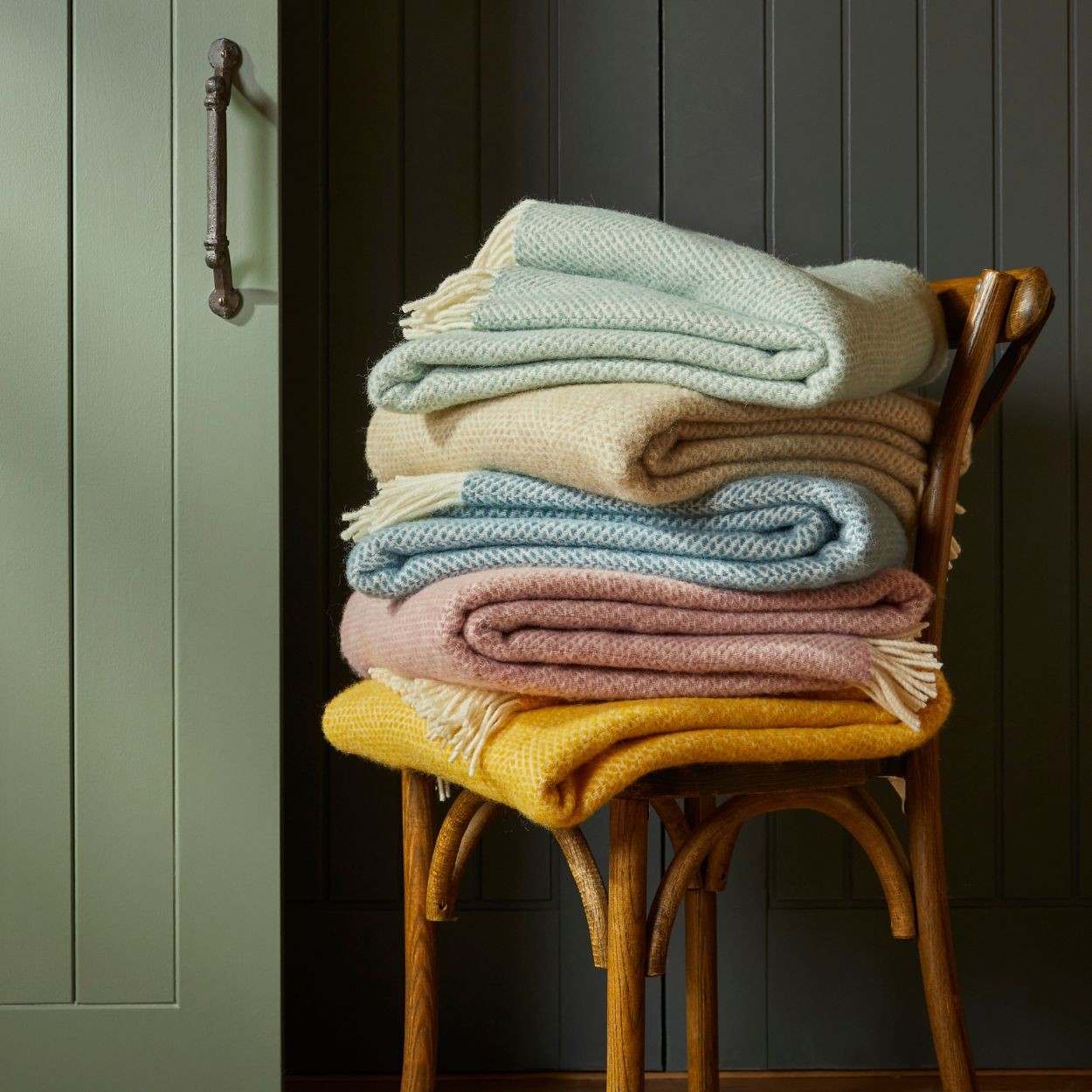 Stack of folded blankets on a wooden chair against a dark paneled wall.
