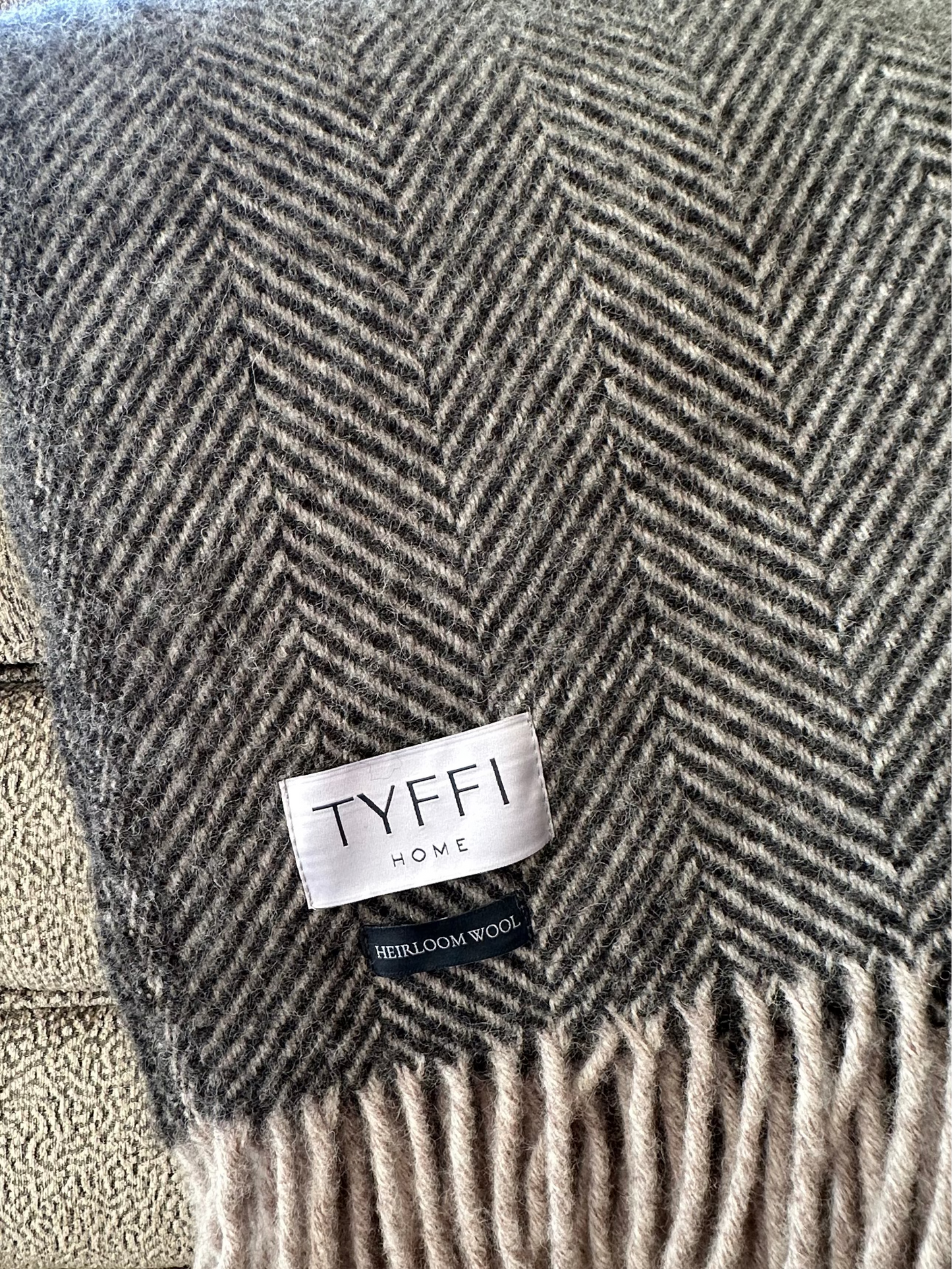 Gray and beige herringbone patterned throw blanket with 'Tyffi Home' label on a textured surface.