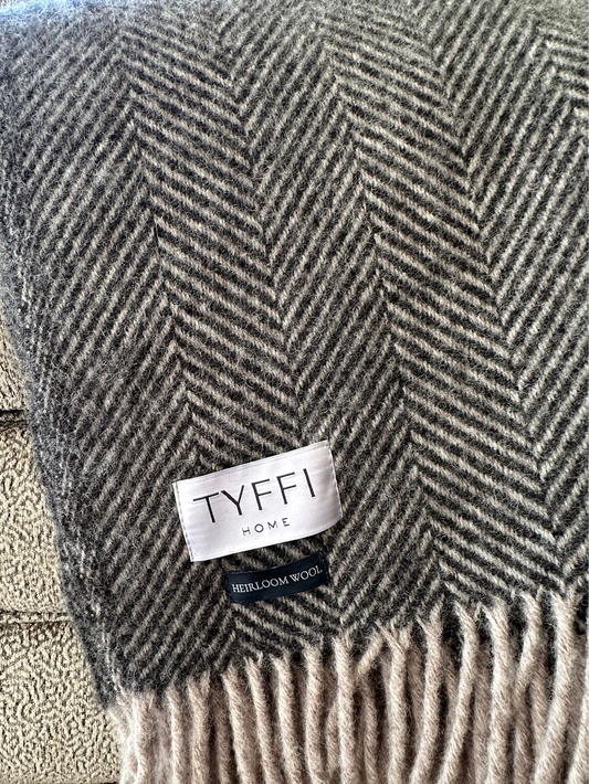 Gray and beige herringbone patterned throw blanket with 'Tyffi Home' label on a textured surface.
