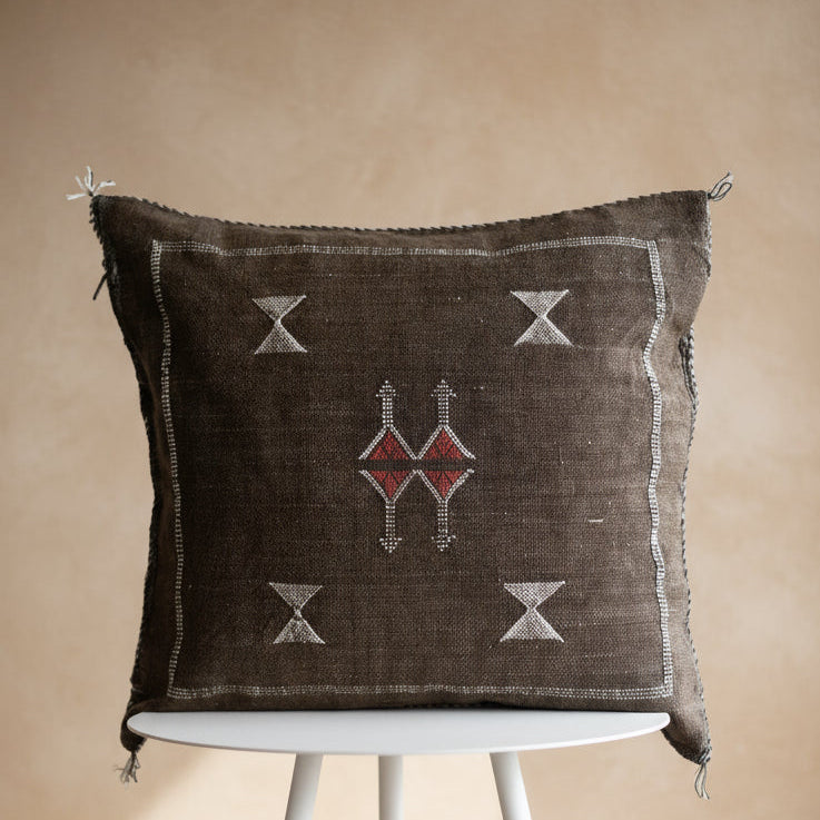 Decorative pillow with geometric patterns on a white stand against a textured white wall