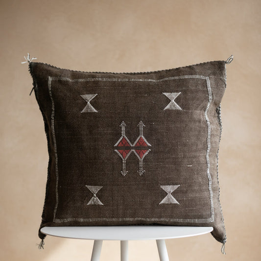 Decorative pillow with geometric patterns on a white stand against a textured white wall