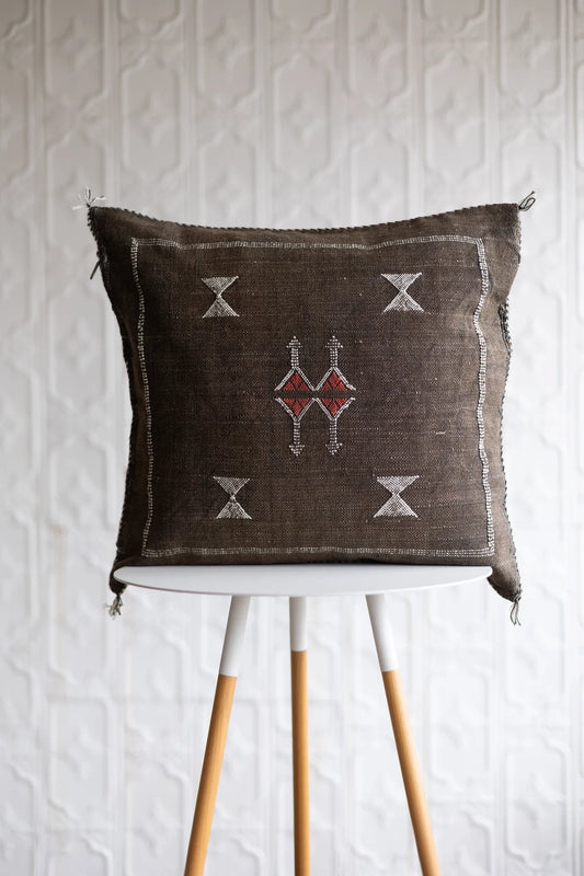 Decorative pillow with geometric patterns on a white stand against a textured white wall