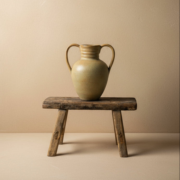 vintage vase with handles on a wooden stool against a plain background
