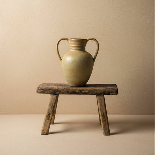 vintage vase with handles on a wooden stool against a plain background