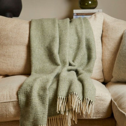 Green blanket draped over a beige sofa with a neutral background
