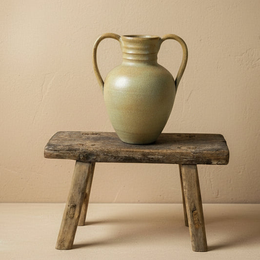 vintage vase with handles on a wooden stool against a plain background