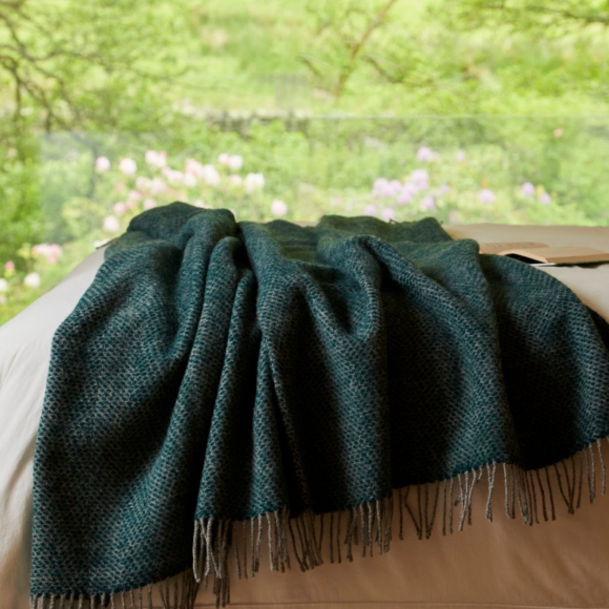 Green blanket with fringes draped over a surface with a blurred natural background